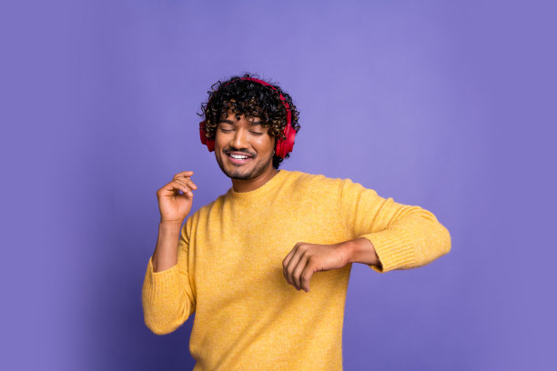 照片中，开朗有趣的男人穿着时髦的黄色衣服，听着音乐，现代科技隔绝在紫色的背景上图片下载