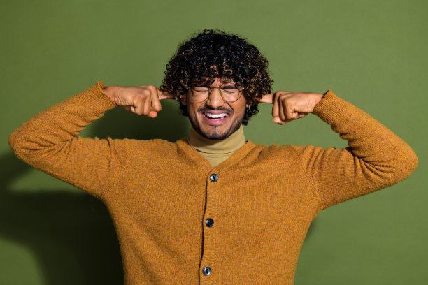 英俊的年轻人的照片肖像手指遮住耳朵避免噪音穿着时髦的棕色服装孤立在卡其色的背景图片下载