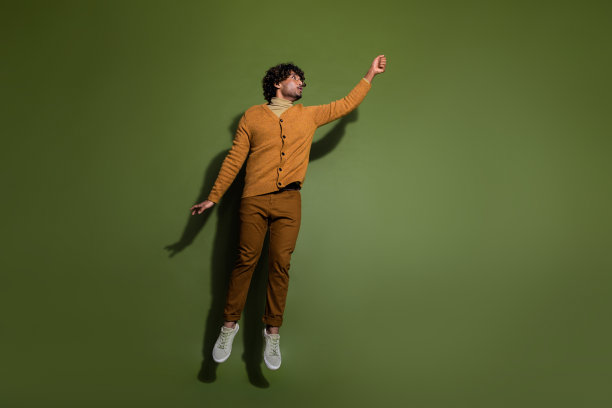 漂亮的年轻男性的全身照片挂空空间穿着时髦的棕色衣服孤立的卡其色背景图片下载