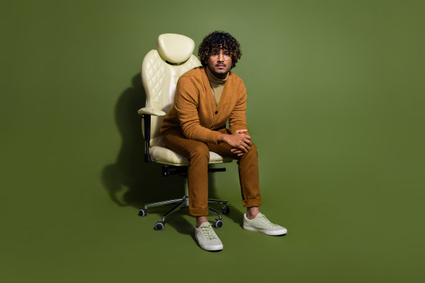 有魅力的年轻人全身照片坐在办公室扶手椅严肃的老板穿着时髦的棕色衣服孤立在卡其色背景图片下载