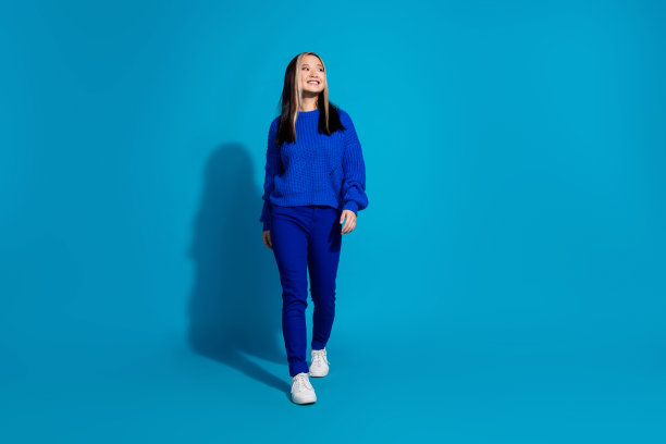 照片年轻的时尚女孩在秋季的服装和白色运动鞋感兴趣地看着新店在蓝色背景下孤立行走图片下载