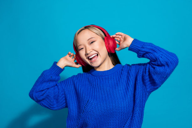 照片肖像的日本女孩穿着时髦的针织时尚套头衫meloman音乐爱好者在耳机孤立的蓝色背景图片下载