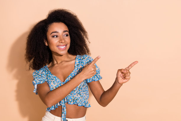 照片中迷人的积极的女人穿着蓝色的上衣指着两根手指，空白的空间孤立的米色背景图片下载