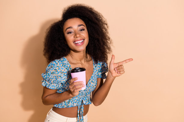 照片中穿着蓝色衬衫的开朗漂亮的女士享受着咖啡，显示出空旷的空间孤立的米色背景图片下载