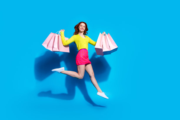 漂亮的年轻女孩跑步的全尺寸照片，拿着购物袋，兴奋地穿着时髦的黄色衣服，孤立在蓝色背景上图片下载