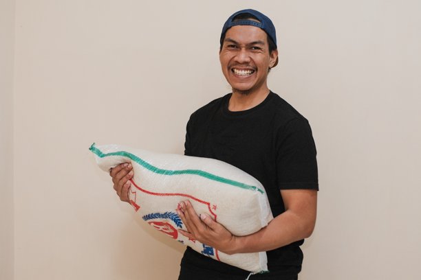 一名东南亚男子在仓库里搬运米袋。图片下载