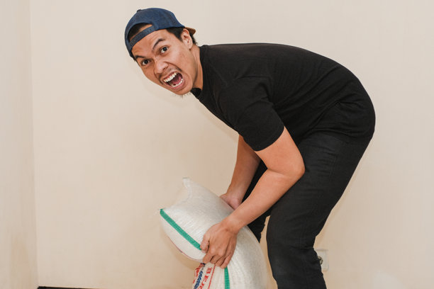 一名身穿黑色t恤、头戴帽子的东南亚男子拎着一个米袋图片下载