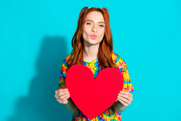 照片肖像迷人的年轻女子亲吻的嘴唇抱着大心脏穿着时尚的彩色衣服孤立的青色背景图片下载