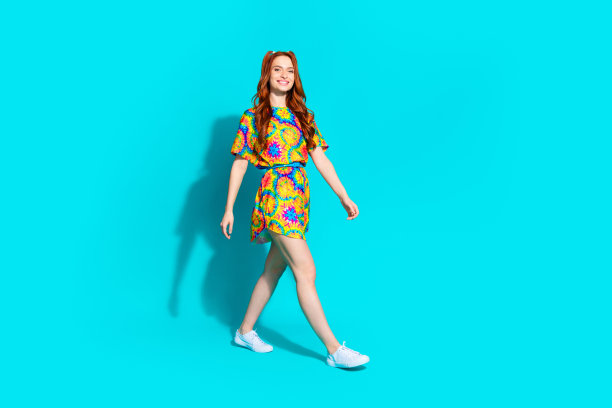 漂亮的年轻女孩走路的全尺寸照片，心情好，穿着时髦的彩色服装，孤立于海蓝宝石色背景图片下载