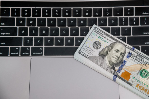 笔记本电脑键盘上的一叠100美元钞票象征着财务上的成功、数字交易和在线业务。是推动电子商务和现代金融服务的理想场所。图片下载