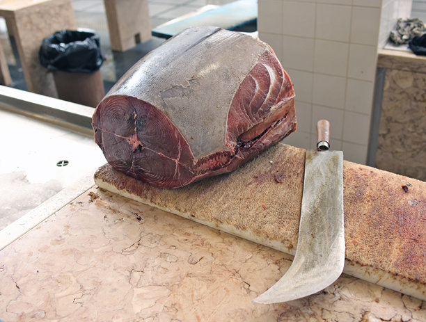 市场鱼贩桌上的一块新鲜金枪鱼和一把切肉刀图片下载