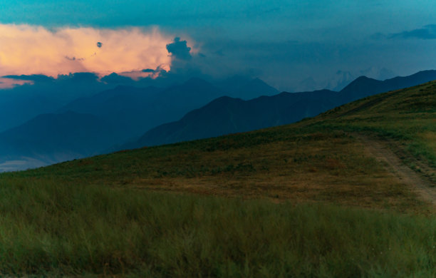 云是一个笑脸。从路边的小山上俯瞰一片明亮的大云，被夕阳的光线染成了颜色，远处是高山。云朵的右边露出了一丝微笑。水平的照片。图片下载