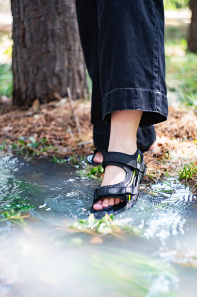 一个穿着黑色牛仔裤和黑色凉鞋的女人的腿特写，脚趾浸在水里。垂直的照片。图片下载