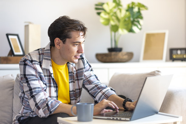 穿着黄色t恤的帅哥在家办公室用笔记本电脑工作图片下载