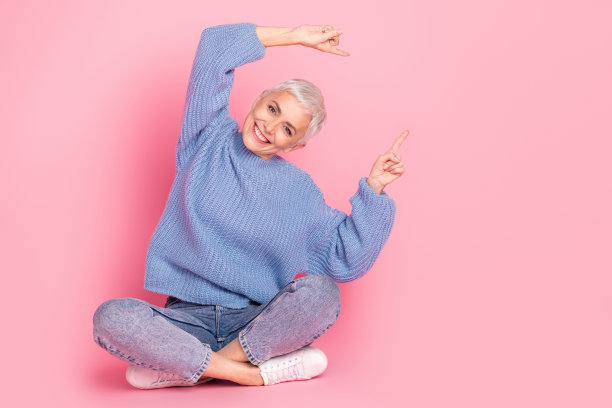 漂亮的退休女性的全身照片坐在地板点空空间穿时髦的蓝色针织服装孤立在粉红色的背景图片下载