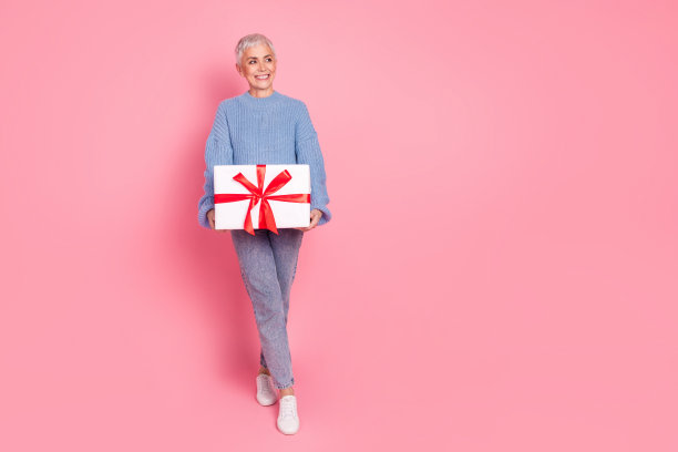 全尺寸照片的高级妇女看空空间拿礼物穿着时尚的蓝色针织品衣服孤立在粉红色的背景图片下载