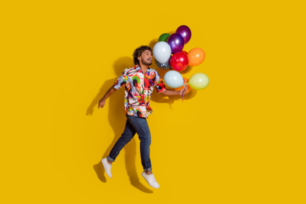有魅力的年轻人手持气球奔跑的全身照片，穿着时尚的彩色衣服，孤立在黄色的背景上图片下载