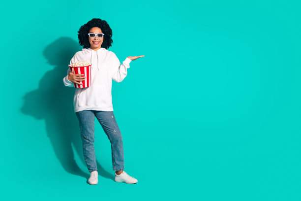 波浪黑发女孩的照片在白色卫衣和3d眼镜吃爆米花宣传新的首映孤立的青色背景图片下载