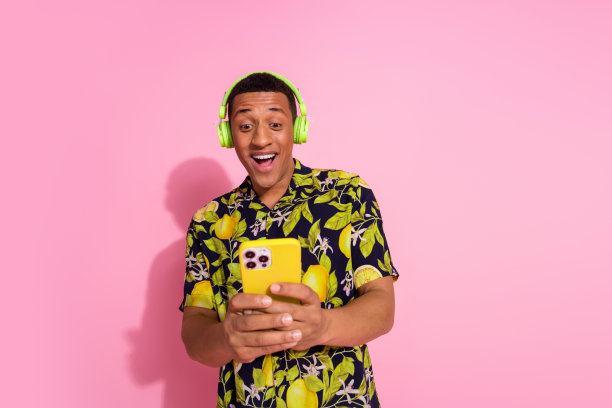 照片肖像英俊的年轻人耳机听音乐设备穿着时尚的热带印花服装孤立在粉红色的背景图片下载