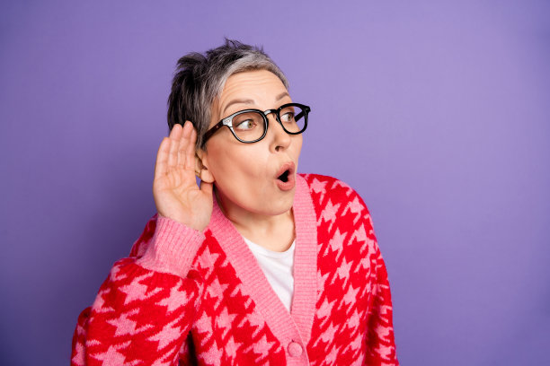 可爱的退休女士的照片肖像手捂耳朵听秘密穿着时髦的红色服装孤立在紫色的背景图片下载