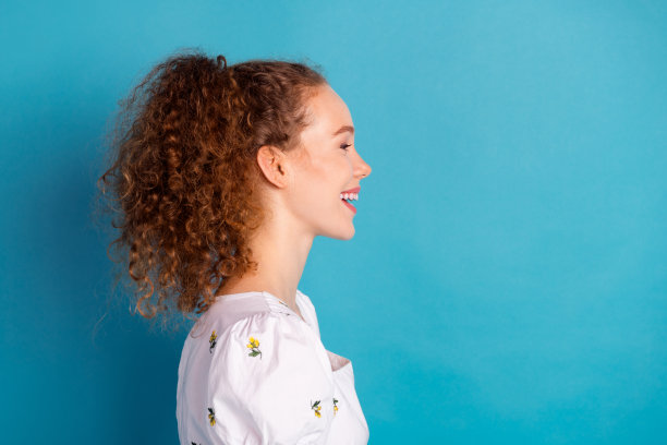 照片中迷人的年轻女子肖像侧面笑空穿着时尚的白色衣服孤立在蓝色的背景图片下载