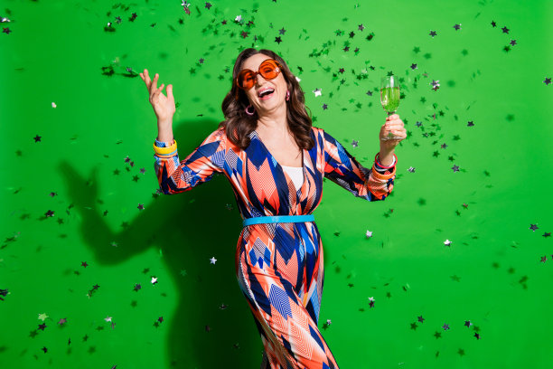 照片中迷人时髦的女士穿着五颜六色的衣服喝酒享受新年聚会空旷的空间孤立的绿色背景图片下载