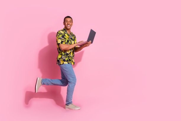 有吸引力的年轻人的全身照片跑拿上网本穿着时尚的热带印花衣服孤立的粉红色背景图片下载