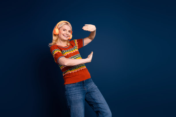 照片中开朗快乐的老年妇女，女人穿着时尚的衣服，有乐趣，听音乐孤立在深蓝色的背景图片下载