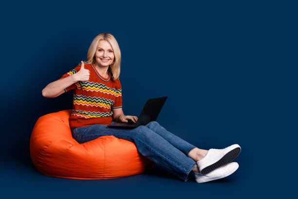 照片迷人华丽的高级妇女穿着时尚的衣服，坐在包拇指向上孤立在深蓝色的背景图片下载