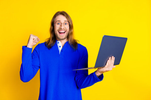 照片中的快乐、开朗、积极的男人穿着时髦的蓝色衣服，套头衫，手握拳头，孤立在黄色的背景上图片下载