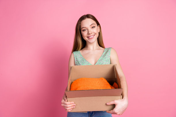 漂亮的年轻女孩拿着衣服盒子的照片，穿在粉红色的背景上图片下载