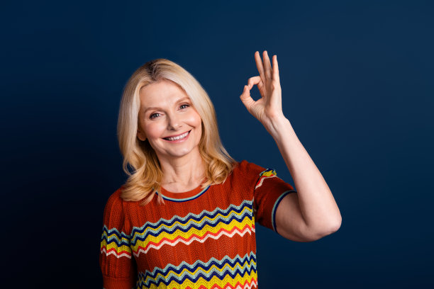 照片中可爱的漂亮女人穿着时尚的衣服，双手ok的标志孤立在深蓝色的背景上图片下载