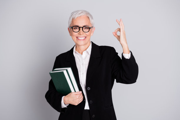 有吸引力的成熟的女性专业教师拿着书的照片显示，她穿着正装，眼镜孤立在灰色背景上图片下载