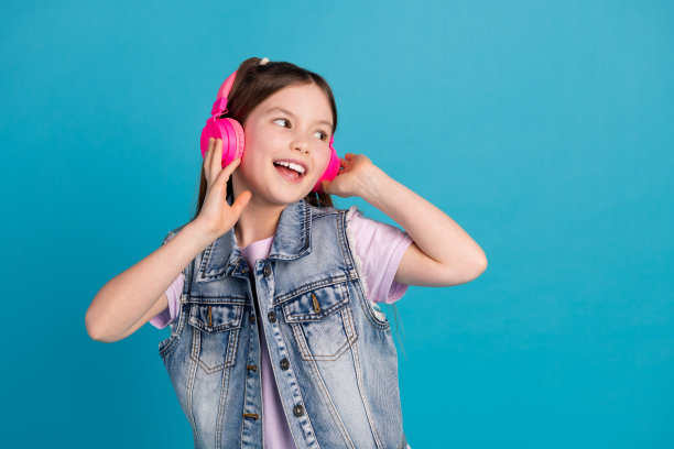 可爱的小女孩的照片耳机听音乐，看空空间穿着时尚的牛仔服装孤立的蓝色背景图片下载