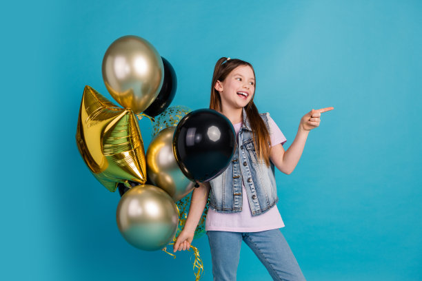 照片中可爱的小女孩手持气球看着点空的空间穿着时尚的牛仔衣服孤立在蓝色的背景图片下载