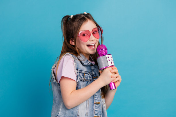 可爱的小女孩唱卡拉ok麦克风的照片肖像穿着时尚的牛仔服装孤立的蓝色背景图片下载