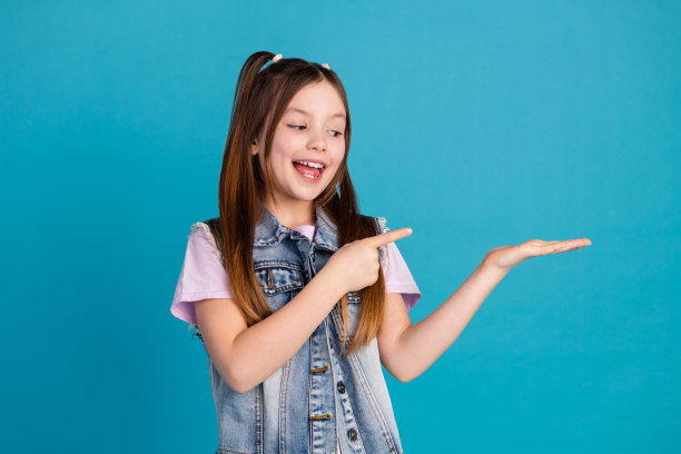 照片肖像可爱的小女孩点抱着看空穿着时尚的牛仔服装孤立在蓝色的背景图片下载