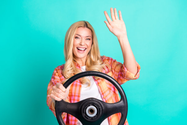 照片肖像可爱的成熟的女士握着方向盘挥手hi穿着时尚的格纹服装孤立的青色背景图片下载