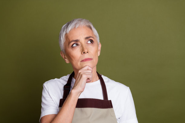照片中体贴迷人的女士穿着围裙，手臂下巴，看起来空白空间孤立的绿色背景图片下载