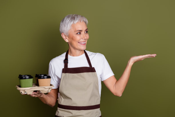 开朗漂亮的女士穿着围裙拿着茶杯的照片，显示手臂空白的空间孤立的绿色背景图片下载