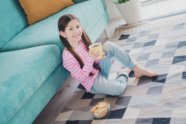 年轻有趣的孩子的照片，棕色头发的小女孩呆在家里，在她的房间里独自喝茶，吃一些糖果饼干图片下载