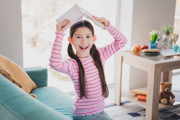 照片肖像的年轻有趣的开玩笑的孩子小黑发女孩呆在家里打开她的头顶上的书孤立在她的房间里图片下载
