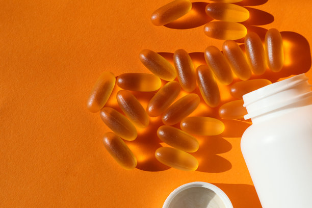 从瓶子里倒出omega - 3胶囊，特写照片，橙色背景。鱼油营养补充剂的顶部视图白色背景。图片下载