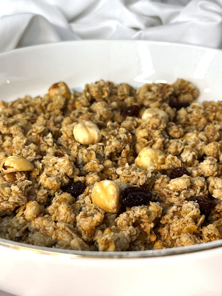 白色的盘子里装着坚果和葡萄干的格兰诺拉麦片，特写在白色的纺织品背景上。图片下载