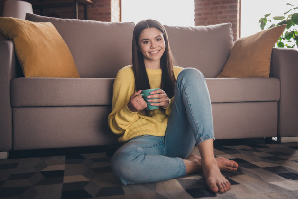 漂亮少女的全身照片坐在地板沙发放松喝茶穿黄色衣服现代室内平坦的室内图片下载