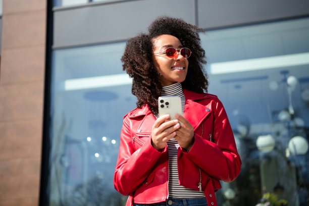 闪亮可爱的女孩穿着红色皮夹克，传达着现代设备走在城市街道上的照片图片下载