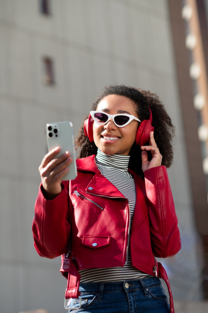 垂直照片的闪亮可爱的女孩穿着皮革红色夹克享受音乐耳机现代设备户外城市街道图片下载