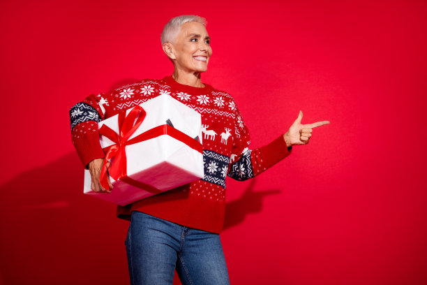 可爱的退休女士的照片看着点空的空间拿着礼盒穿印花毛衣庆祝新年孤立的红色背景图片下载