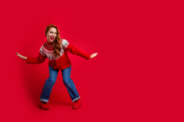 照片的年轻红发女士穿着丑陋的毛衣跳舞的布吉伍吉迪斯科主题派对孤立的红色背景图片下载
