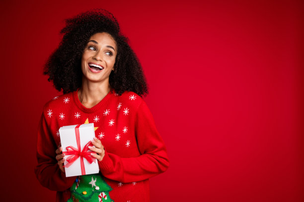 欢快可爱的女孩穿着时髦丑陋的装饰套头衫的照片，节日活动出售空空间孤立在红色背景上图片下载